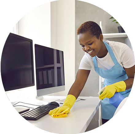 Smiling female cleaner using commercial cleaning products to properly disinfect a computer monitor in an office environment.