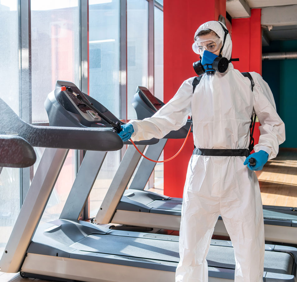 Commercial cleaner in hazmat suit disinfecting gym equipment.